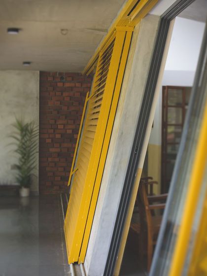 A detail of the angled, yellow louvered shutters. This custom element serves as a functional sunshade and a vibrant sculptural feature against the raw concrete wall.