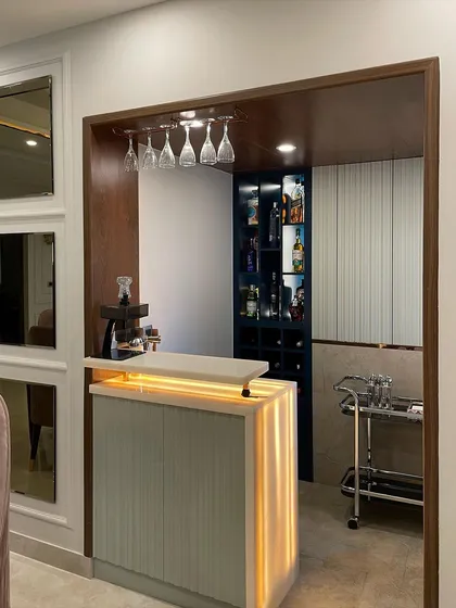 This home bar nook features a backlit Onyx counter that creates a warm, inviting glow. We paired it with a dark blue shelving unit and an overhead wine glass rack to create a compact yet fully functional bar area.