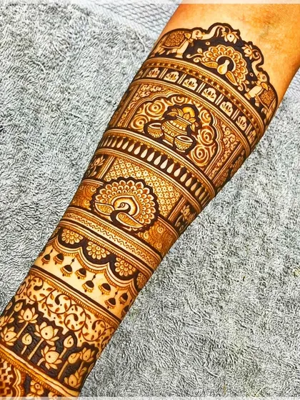 A detailed view of a forearm design, featuring beautiful peacock and kalash (pot) motifs.