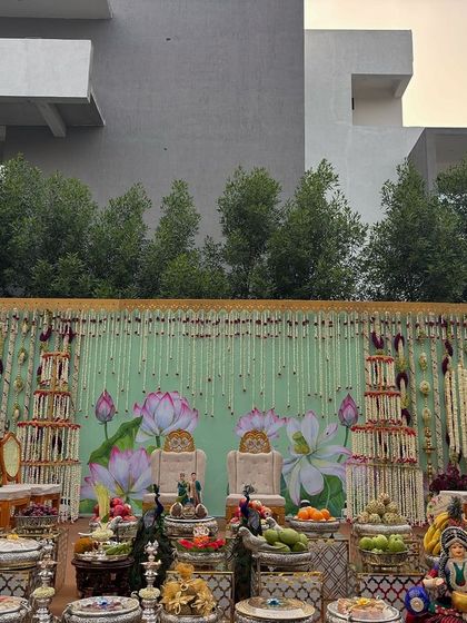 An outdoor ceremony setup against a modern building, with a beautiful lotus-themed backdrop and hanging garlands.