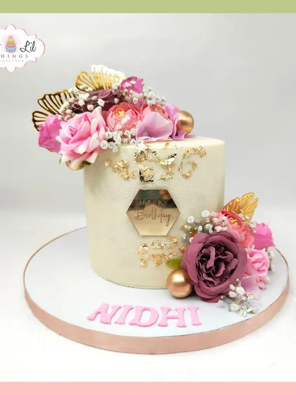 A beautiful floral birthday cake for Nidhi, topped with a crown of pink roses and gold details.
