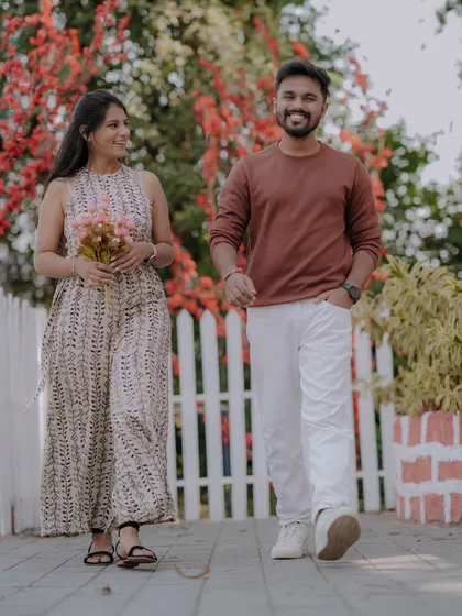 A casual stroll hand-in-hand along a path lined with a white picket fence and vibrant flowers. This image captures the simple, everyday romance that is the foundation of a great love story.