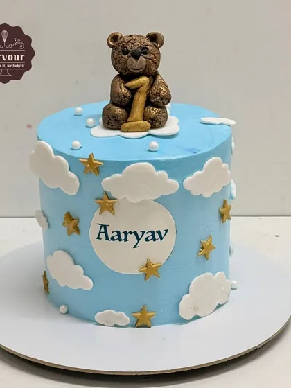 A sweet first birthday cake with a teddy bear on top. This blue cake is decorated with clouds and stars, perfect for a little boy's celebration.