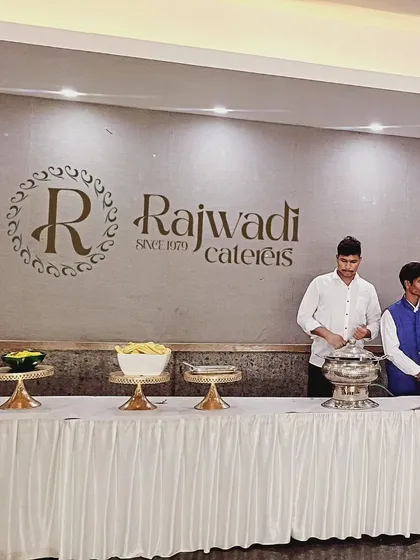 My team is ready to serve at a corporate lunch, positioned before a clean buffet line and our official "Rajwadi Caterers Since 1979" branding. This reflects my long-standing commitment to professional service.