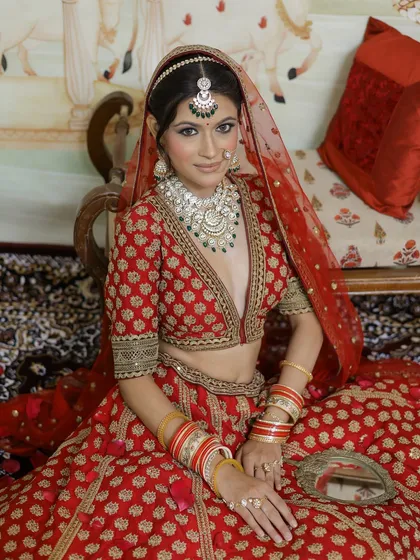 Seated in a regal pose, this bride embodies traditional grace. Her makeup is kept classic with a defined eye and a flawless base, ensuring she looks perfect from every angle.