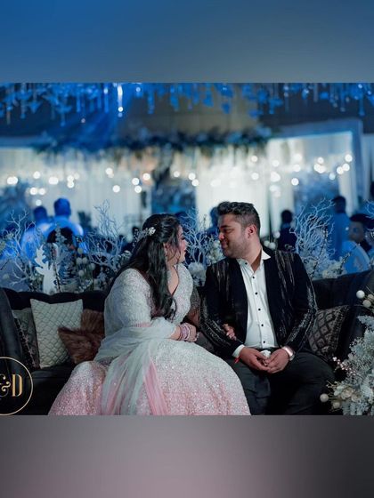 The couple enjoying their winter-themed event. They are seated amidst decor featuring white frosted branches and cool-toned florals, creating a romantic and magical winter atmosphere.