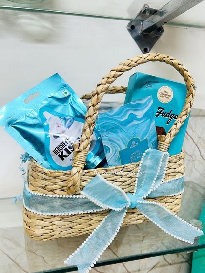 A close-up of the new mom hamper, showing the handwoven basket filled with blue-themed goodies like Hershey's Kisses and The Cinnamon Kitchen fudge.