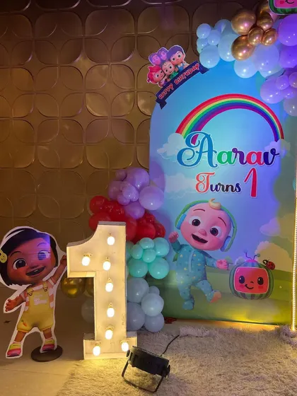 This is a duplicate of ID 1, 68, 137, 184, 226, 213, 240, 250. A vibrant Cocomelon theme for a first birthday party. This setup includes a custom arched backdrop, a rainbow-colored balloon arrangement, and a life-sized cutout of the character JJ.