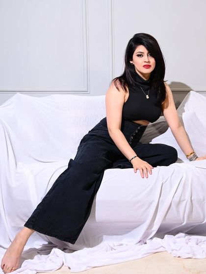 A powerful and edgy shot of a model in an all-black outfit, posing on a white-draped sofa.
