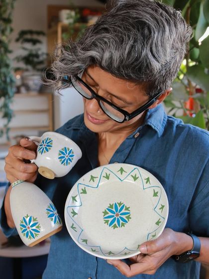Admiring the finished pieces from a student's collection, featuring beautiful hand painted floral motifs on a plate, tumbler, and mug.