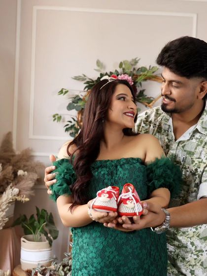 Holding tiny red shoes, a symbol of the little feet that will soon be running around. A heartwarming and creative shot.