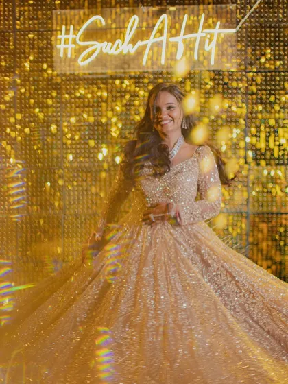 The bride twirls in her shimmering gown in front of a custom neon sign and a glittering gold backdrop. A perfect shot for a glamorous cocktail night.