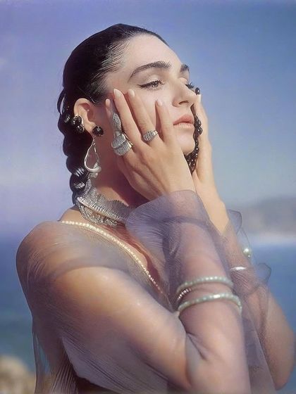 An ethereal portrait of Kavya Trehan against a soft, painted sky. The sheer fabric and delicate jewelry add to the dreamlike quality of the image.