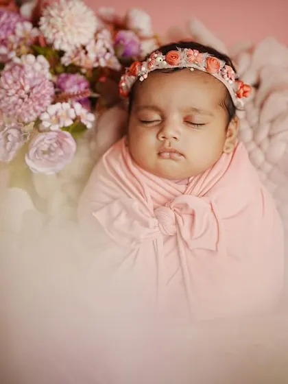 A dreamy, soft-focus shot of a newborn girl surrounded by flowers. The artistic blur in the foreground adds a magical quality to this infant portrait.