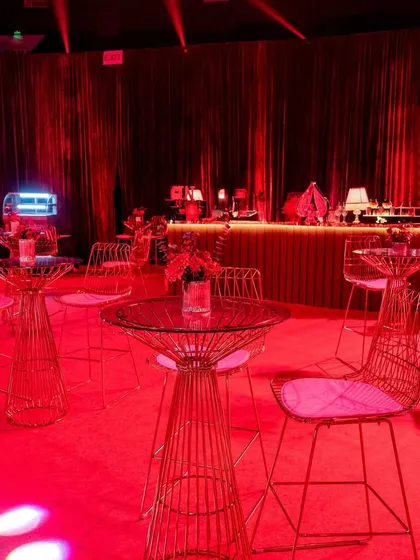 The bar area was designed with modern, minimalist furniture to contrast with the opulent decor. Gold wireframe high-top tables and chairs stood against a backdrop of pleated red curtains and a warmly lit bar.