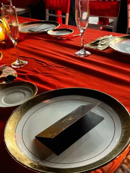 A stunning table setting for a sit down dinner reception. The bold red tablecloth, elegant glassware, and personalized menus create a romantic and luxurious ambiance for the guests.