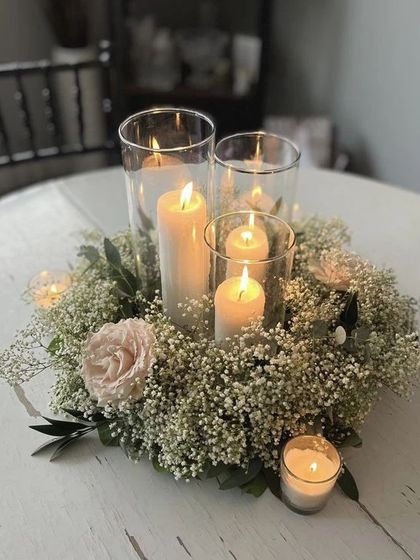 A romantic candle and floral centerpiece. The arrangement of baby's breath and a single pink rose around the candles creates a soft and intimate table setting.