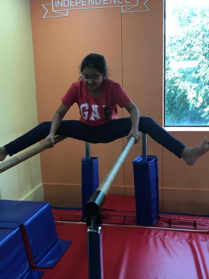 This grade-schooler shows impressive flexibility and strength, holding a straddle position on the parallel bars, a testament to her hard work and practice.