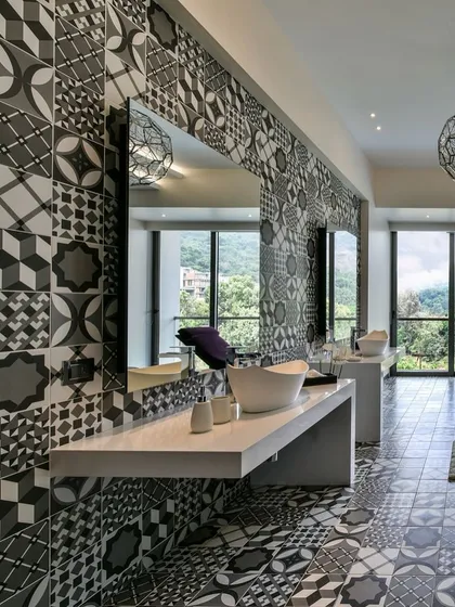 This bathroom in a Khandala villa uses bold black and white patterned tiles on both the floor and the feature wall. The floating concrete vanity and large mirrors create a sense of space, while the windows offer a view of the lush green landscape.