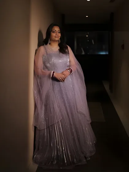 A full-length shot in a hallway. The simple, elegant lines of her gown are complemented by a soft and timeless makeup look.