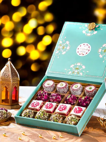 A beautiful turquoise Diwali gift box filled with artisanal sweets, styled with a lantern and diyas. The moody lighting and rich colors create an elegant and festive atmosphere.
