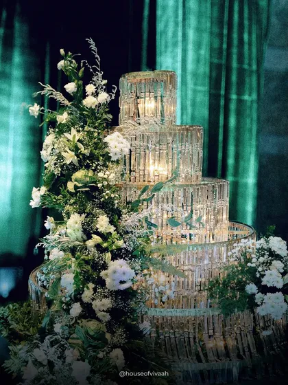 A multi-tiered crystal installation, illuminated from within and adorned with white florals, stands as a beacon of glamour and luxury at this elegant evening event.