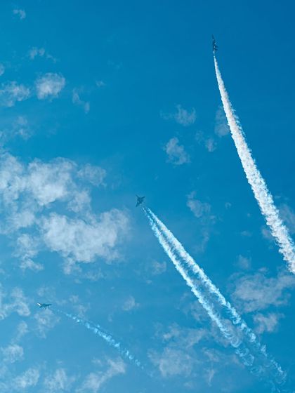 A dynamic shot of jets performing aerobatics, leaving curving smoke trails across the sky.