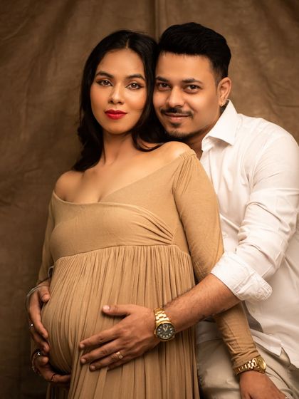 A classic and elegant studio portrait of an expecting couple. Their direct gaze and loving embrace convey a sense of confidence and shared joy.