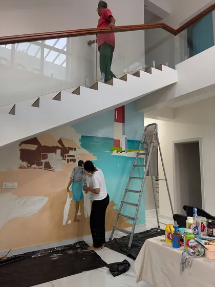 No wall is too tricky, not even a double-height staircase. Here you can see my team and I working on a large beach-themed mural for a client's home, bringing coastal vibes indoors.