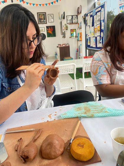 A participant uses a tool to add texture to her clay pot. The workshop covers various techniques to help you personalize your creation.