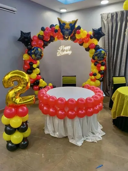 A 'Transformers' or robot-themed second birthday. The balloon arch in red, yellow, and black is topped with a character foil balloon, with a matching number '2' balloon column.