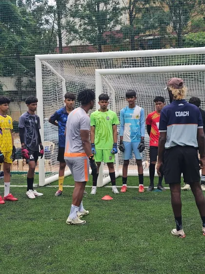 A coach provides direct instruction to a group of aspiring goalkeepers on the training pitch. We emphasize small group coaching to ensure every player gets personalized feedback and guidance.
