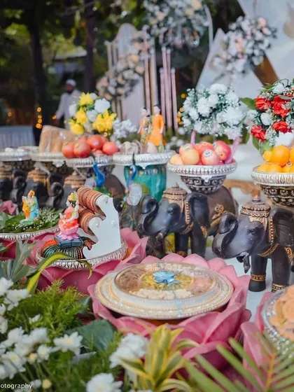 A close-up of an offering table with elephant props, a Ganesha idol, and bowls of fresh fruit.