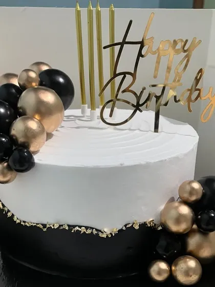 This black and gold themed cake is the definition of chic. The elegant design features a clean white top, a contrasting black base with gold leaf, and balloon-like spheres, perfect for a sophisticated birthday celebration.