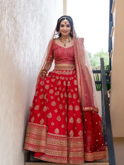 A beautiful solo portrait of the bride in her stunning red lehenga. This posed shot on the stairs showcases her complete bridal look, from her jewelry to her radiant smile.