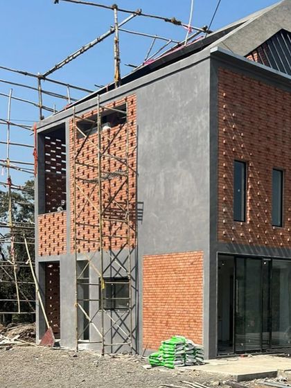 A view of the Kolgaon Masterplan house under construction, highlighting the contrast between solid brick, smooth plaster, and large glass openings. This stage reveals the fundamental material and structural palette of the home.