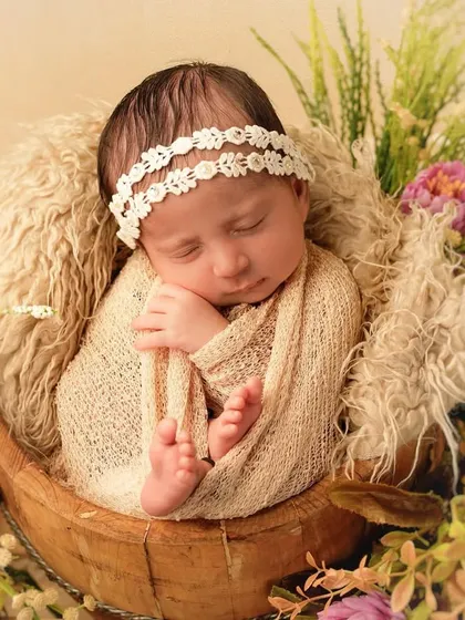 Tucked into a rustic wooden bowl, this sleeping newborn is surrounded by soft textures and florals. We use a variety of props to create beautiful, composed infant portraits that feel both natural and artistic.