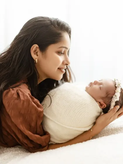 A mother gazes lovingly at her newborn baby, holding her gently in her arms. The bright, airy background keeps the focus on their connection.