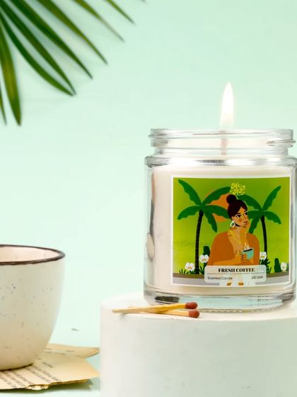 The playful label of this Irish Coffee candle is the star of this clean, modern setup. Paired with a simple ceramic cup and matches on a white pedestal, the image feels fresh, vibrant, and inviting.