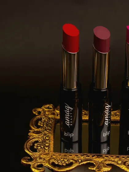 These three lipsticks are presented on an ornate golden tray, creating a look of classic luxury. The dark, moody background makes the vibrant red, mauve, and pink shades appear even richer.