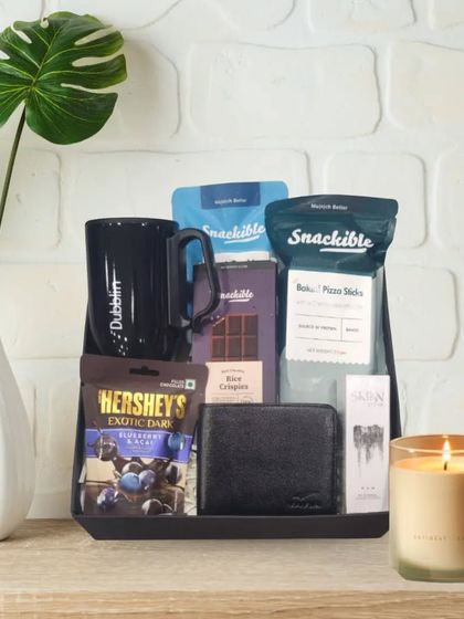 A classic Rakhi hamper for a brother. It features a black tray holding a Dubblin mug, a leather wallet, Skinn perfume, and a variety of chocolates and snacks.
