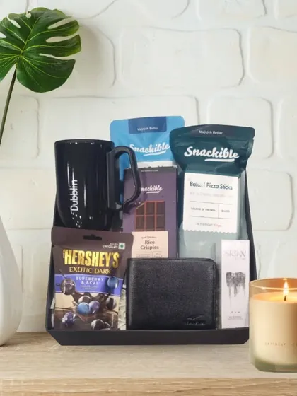 A classic Rakhi hamper for a brother. It features a black tray holding a Dubblin mug, a leather wallet, Skinn perfume, and a variety of chocolates and snacks.
