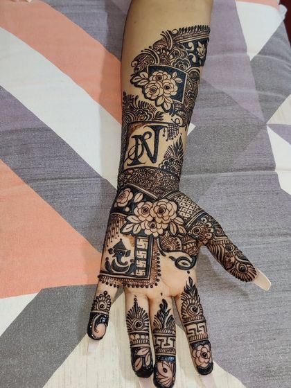A personalized party mehandi featuring the initial "N". The design combines floral elements with auspicious symbols like Ganesha and the swastika.