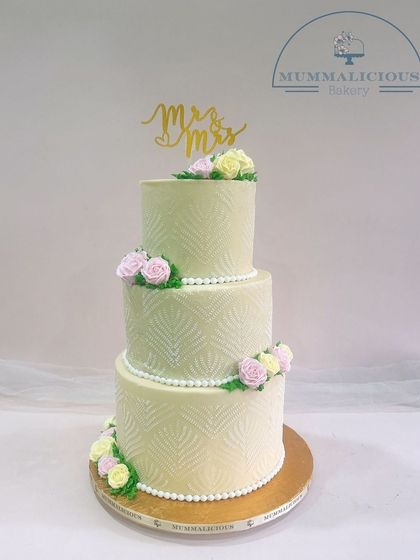 A timeless three-tiered wedding cake in a soft pastel green. The subtle textured pattern, pearl borders, and delicate sugar flowers create a look of classic elegance for your special day.