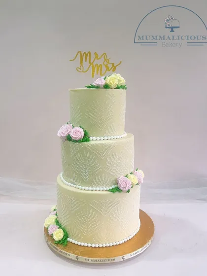 A timeless three-tiered wedding cake in a soft pastel green. The subtle textured pattern, pearl borders, and delicate sugar flowers create a look of classic elegance for your special day.