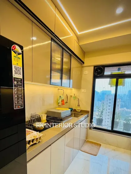 A real-life view of a compact and efficient kitchen. I designed this with glossy white and beige cabinets, a black refrigerator, and profile lighting in the ceiling to make the space feel bright and modern.