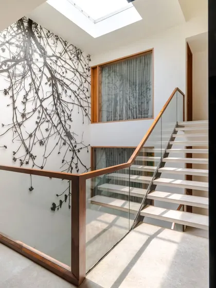 A closer look at the junction where the staircase landing meets the 'Tree of Life' installation. The design uses a simple palette of wood, glass, and white walls to ensure the intricate metal artwork remains the undisputed focal point.