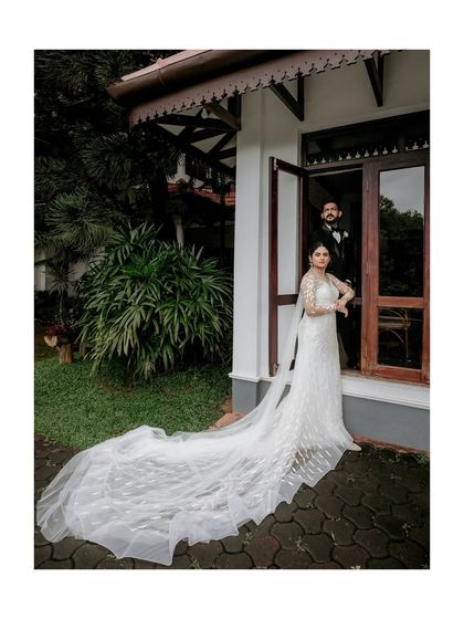 A stunning full-length portrait of the bride and groom, showcasing the magnificent train of her wedding gown against a traditional backdrop.