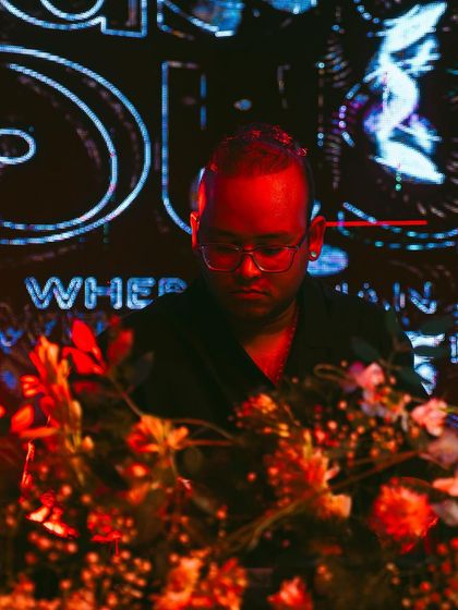 A close-up during my set, bathed in the red and blue light of the 'Masala House' visuals. I focus on weaving a seamless journey through different Indian-inspired electronic tracks.