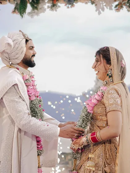 A joyful, candid moment between the couple during their varmala ceremony, with the beautiful mountain landscape visible behind them.